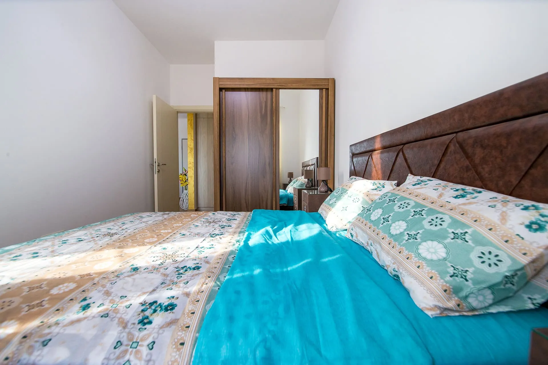 Bedroom featuring a large bed with blue bedding, brown headboard, and wooden wardrobe with mirror.