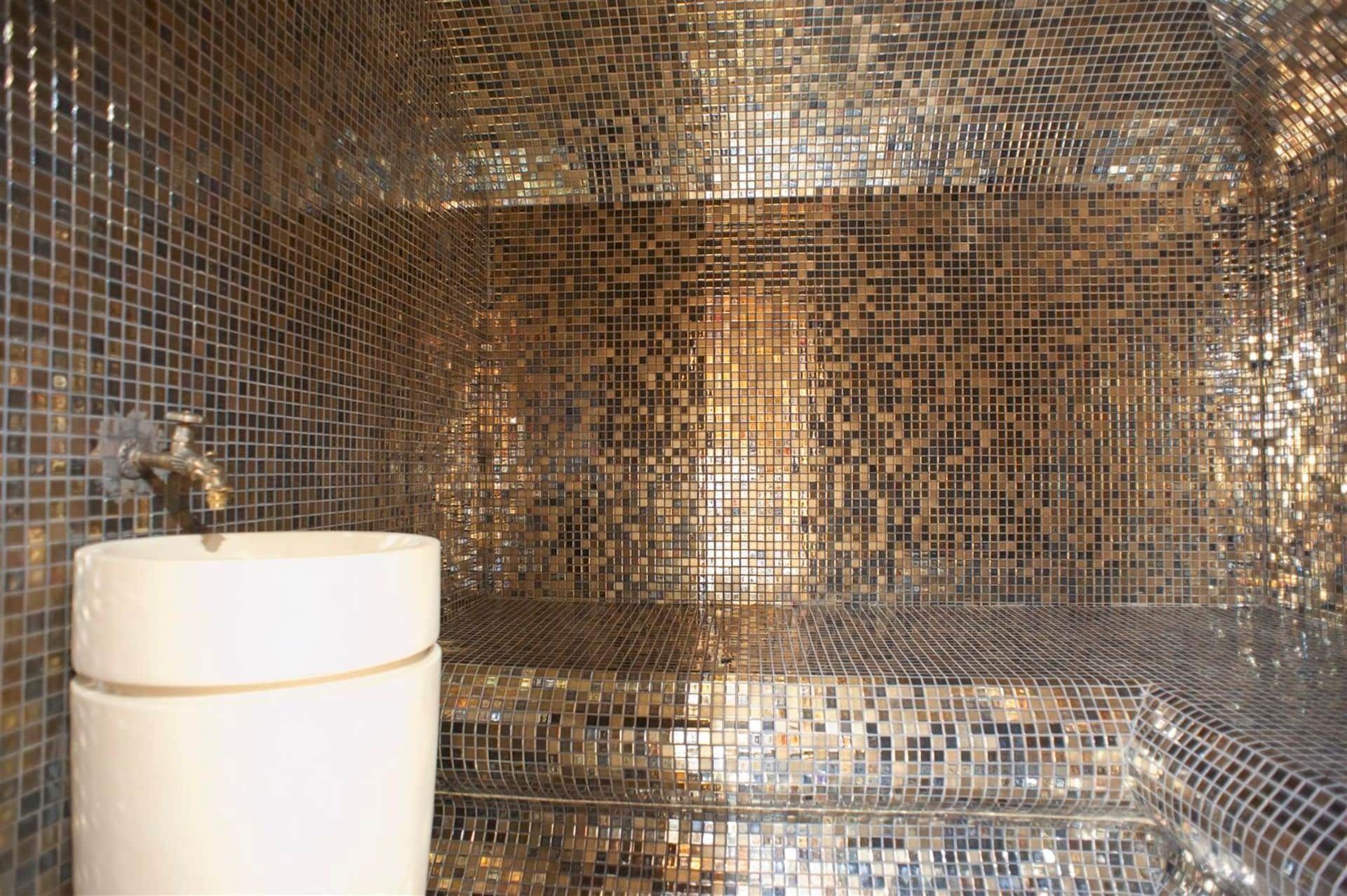 Designer bathroom with gold mosaic finishes and a white sink in a villa in Krašići, Montenegro.