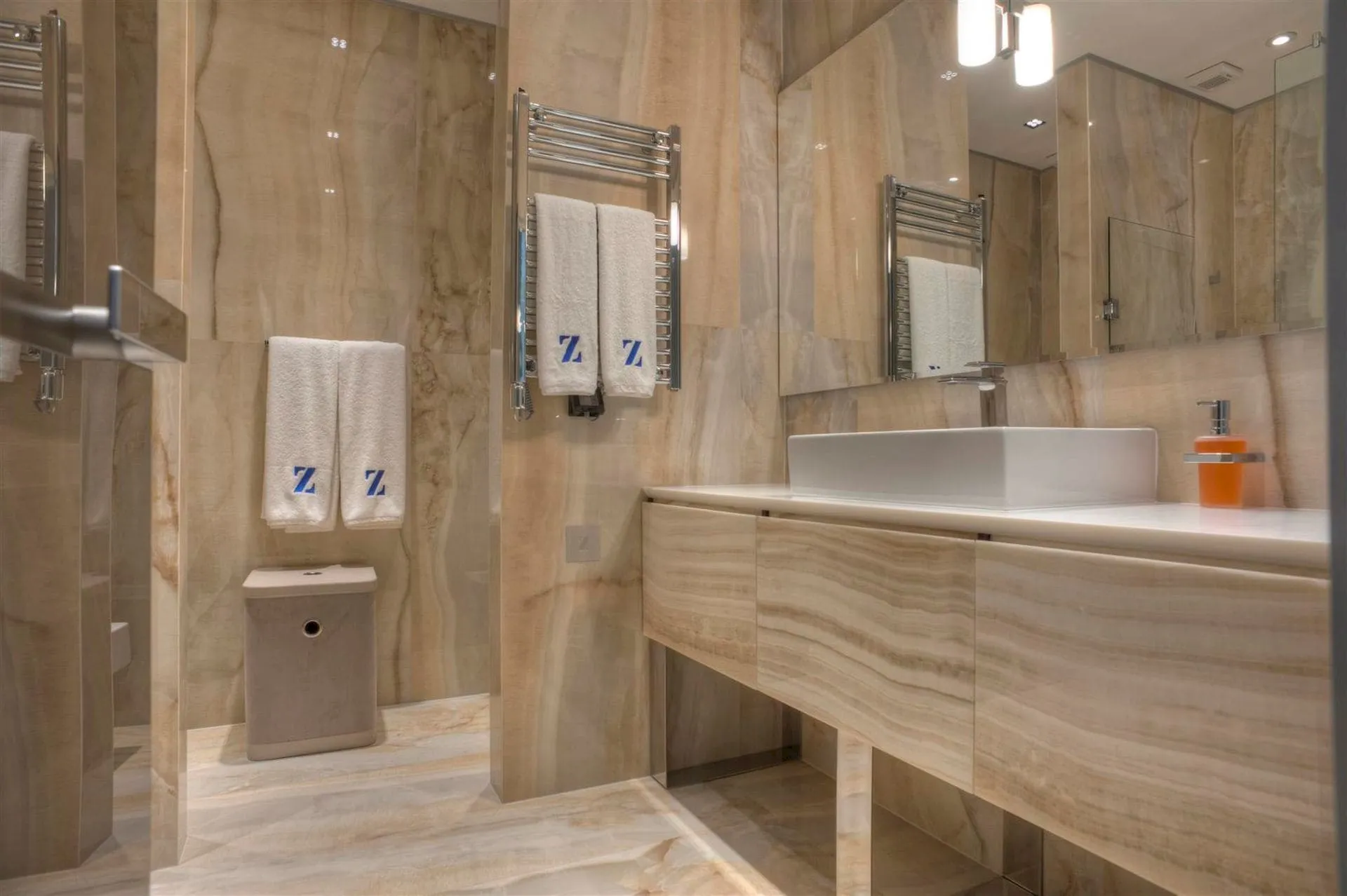 Modern bathroom with marble tiles, floating vanity, vessel sink, heated towel rack, and large mirror.