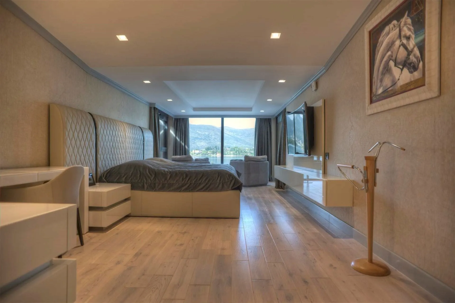 Bright bedroom featuring a large bed, wood flooring, and a panoramic window overlooking mountains.