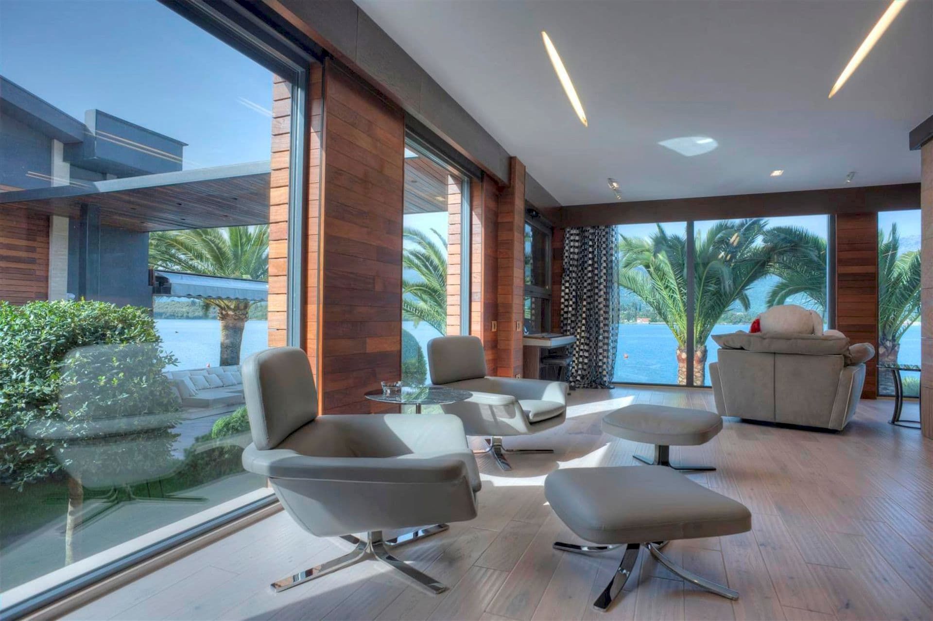 Living room of a modern villa in Krašići, Montenegro: panoramic windows, sea view, wood finishes, and stylish furniture.