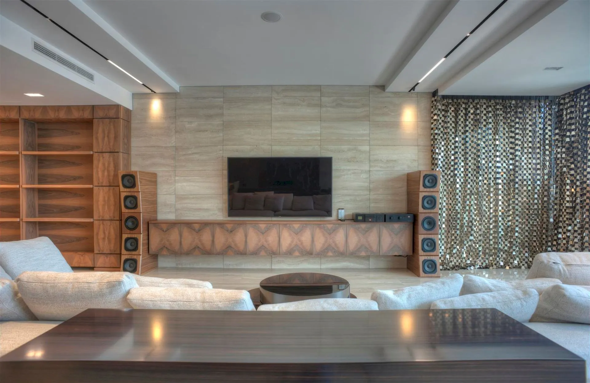Modern living room featuring a sofa, TV on a stone wall, tall wooden speakers, and built-in shelving.