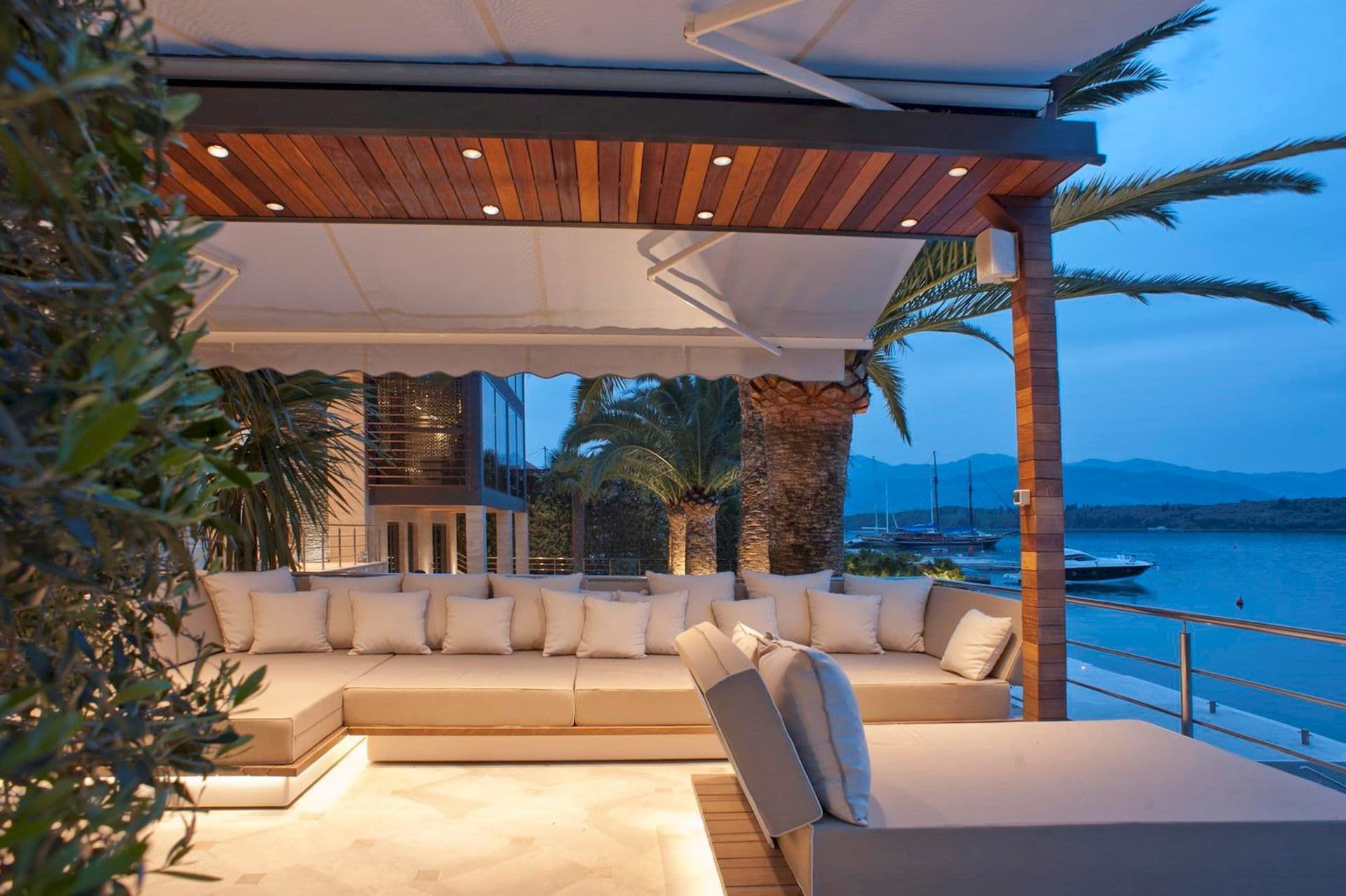Villa terrace in Krašići, Montenegro: soft seating, a wooden ceiling with lighting, and a view of the sea and yachts.
