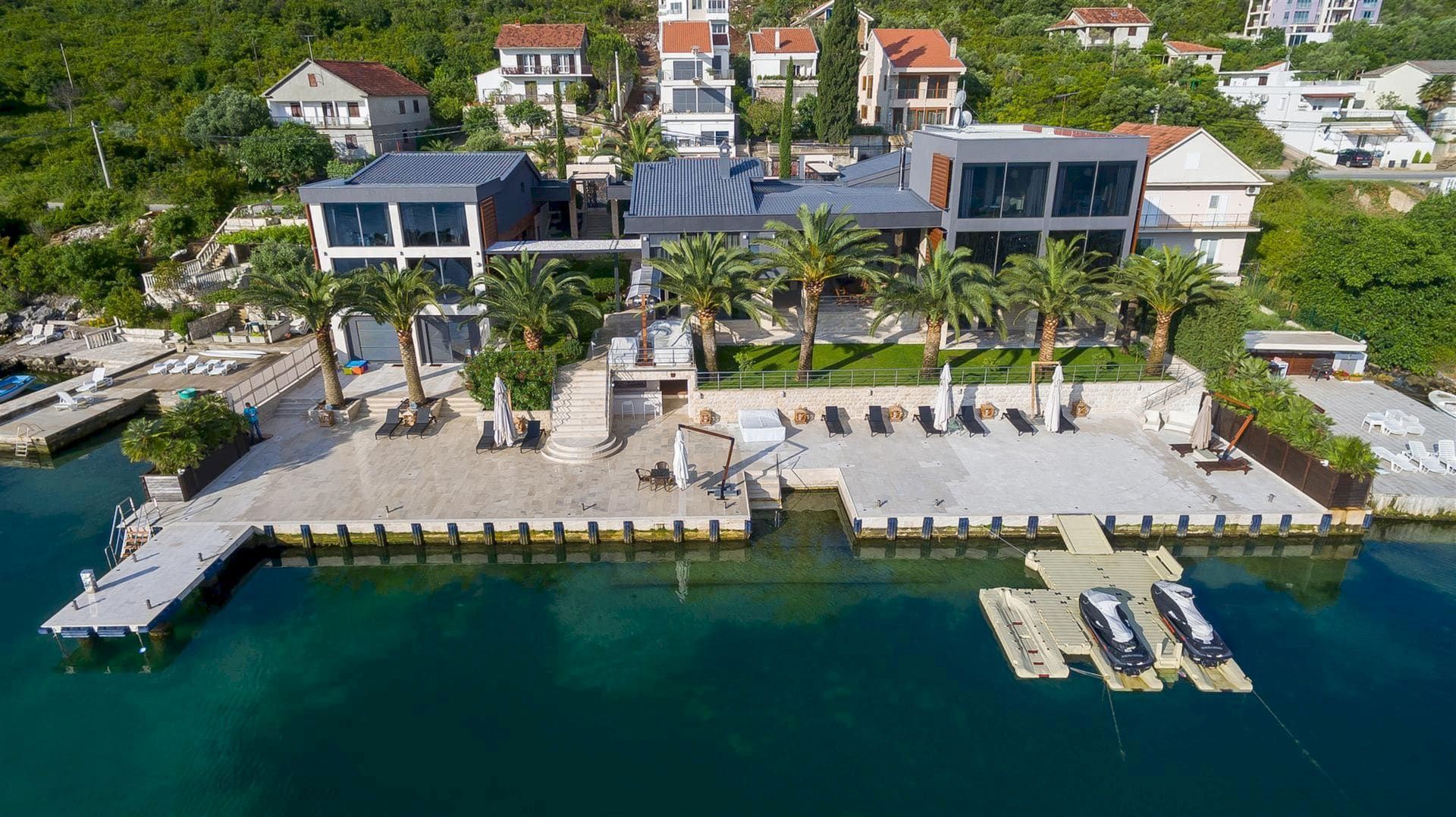 Modern villa in Krašići, Montenegro: panoramic view of the house with its own pier, beach, and palm trees by the sea.