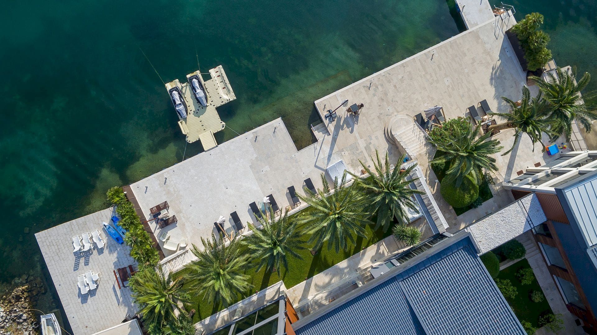 Aerial view of a villa in Krašići, Montenegro: private beach, boat dock, sun loungers, and palm trees by the sea.