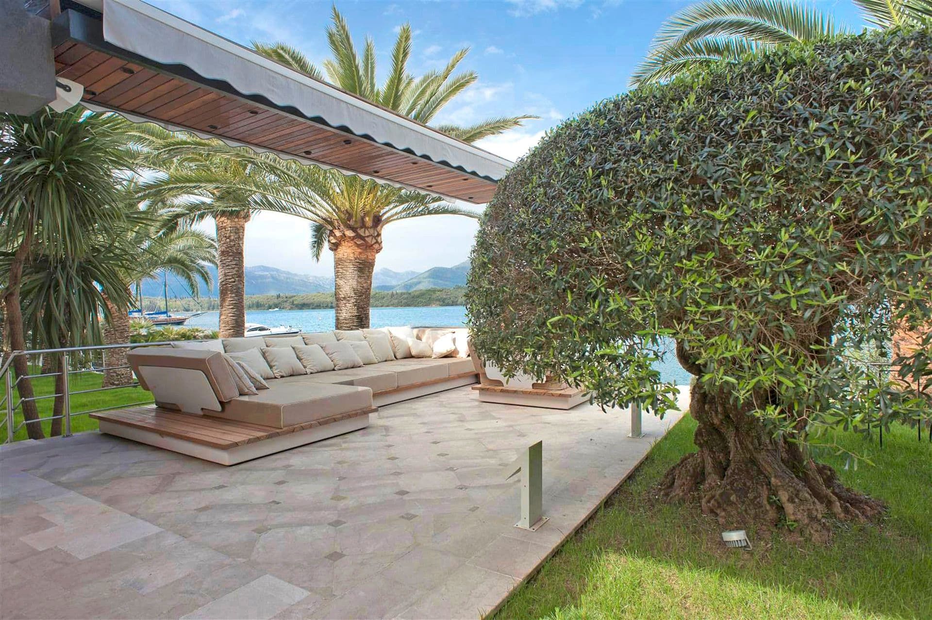 Villa terrace in Krašići, Montenegro: soft seating, sea view, palms and an olive tree by the house.