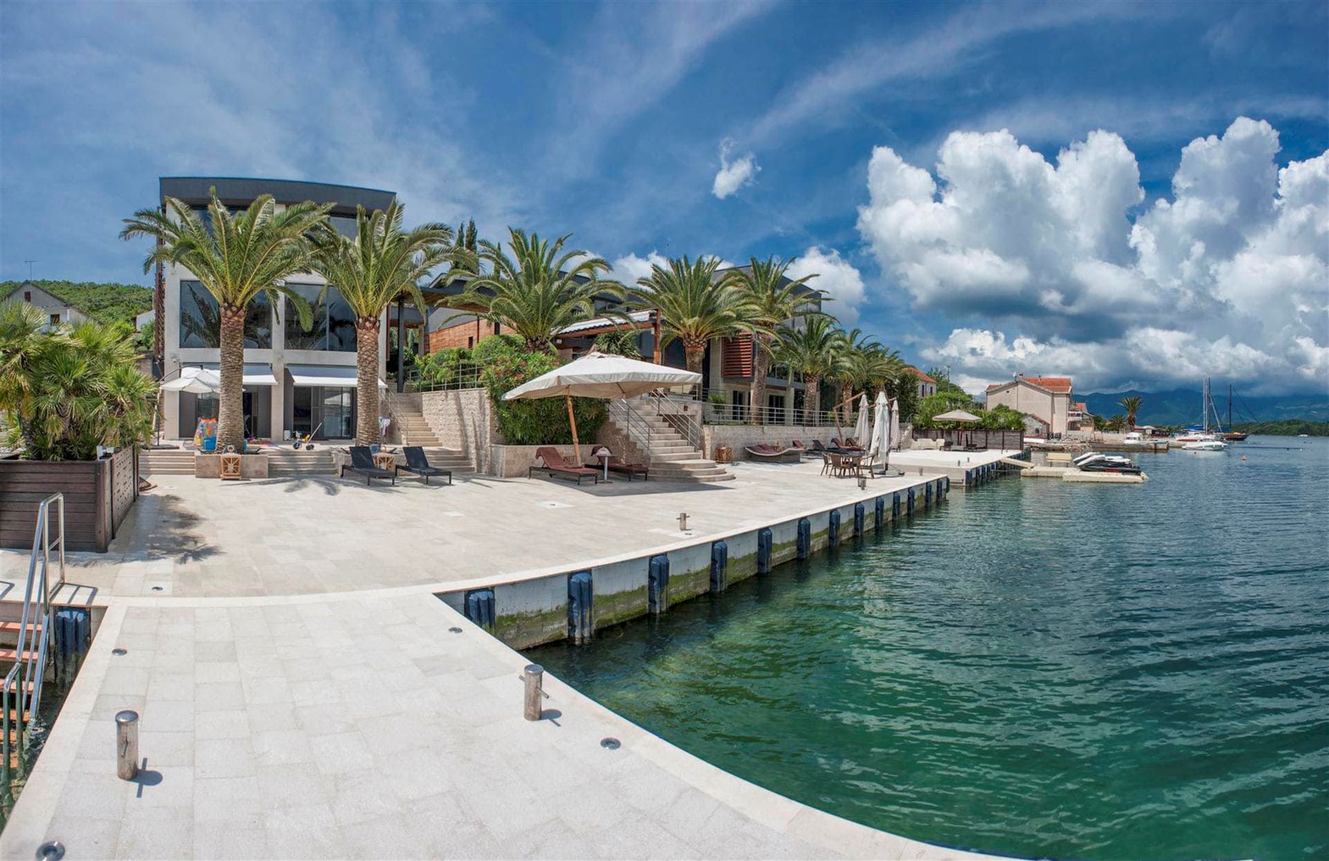 Modern villa in Krašići, Montenegro: private pier, terrace with sun loungers, palm trees, and direct access to the sea.