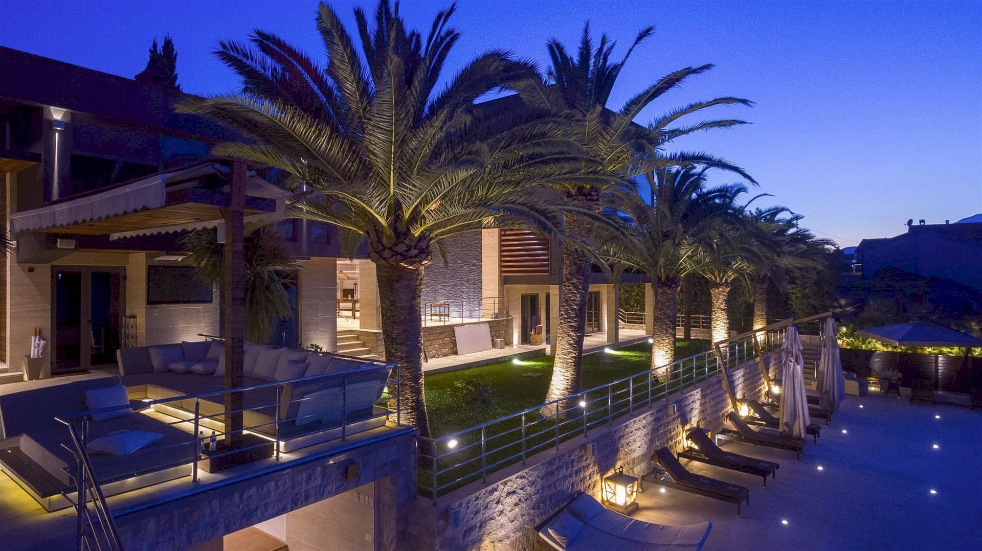 Evening villa in Krašići, Montenegro: terrace with soft seating, palm trees, lighting, and a lounge area by the pool.