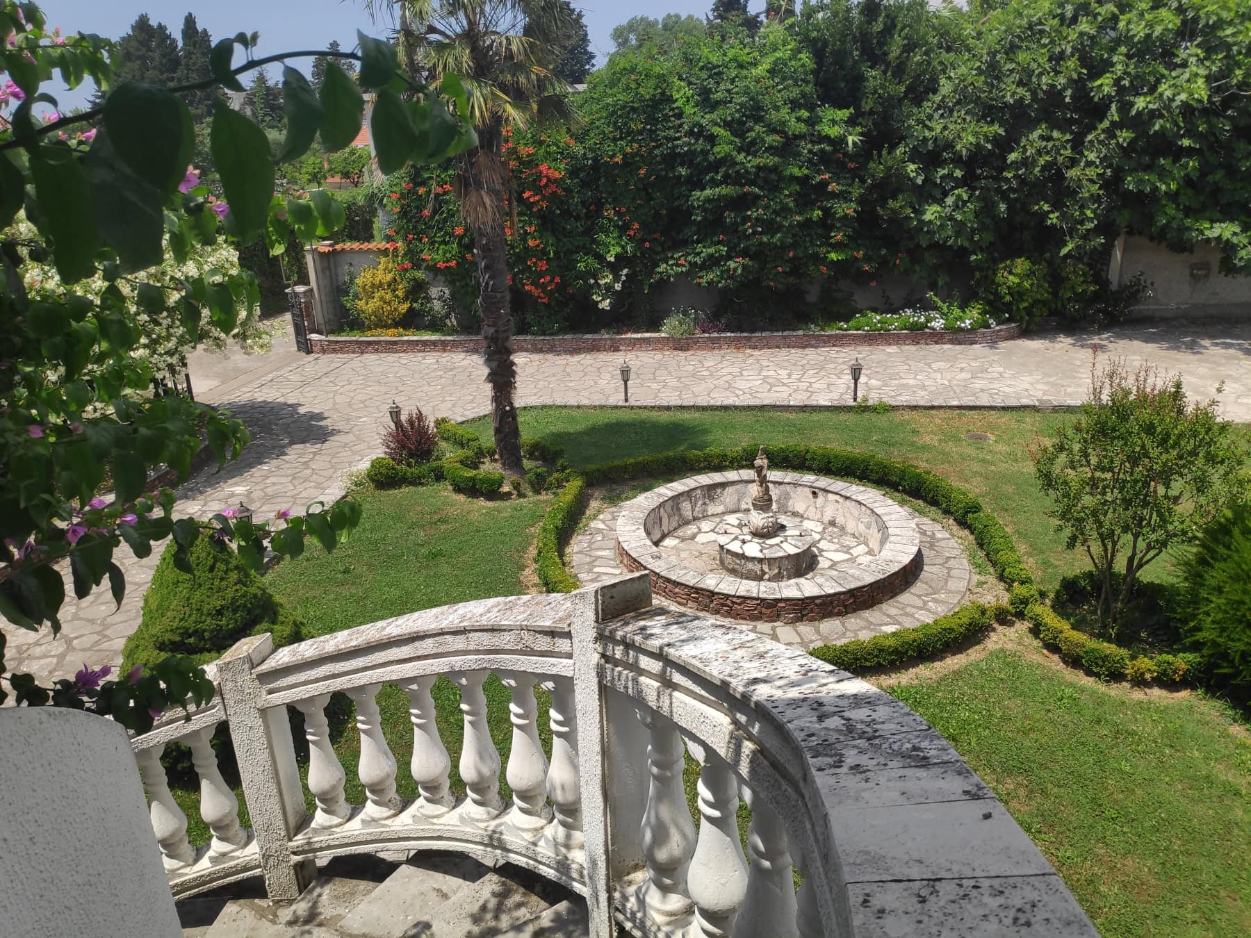 View from the terrace of a green garden with a fountain and stone steps by the house in Bar, Montenegro.