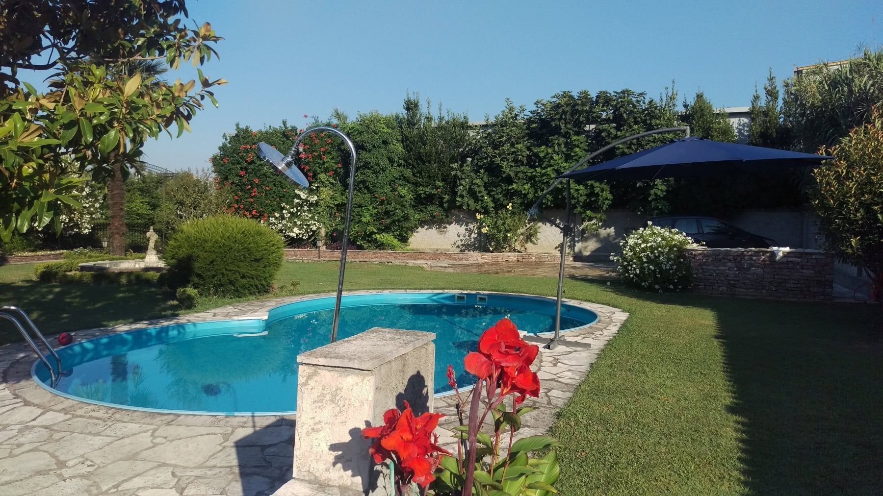 An outdoor pool with a shower and umbrella in the green garden of a private house in Bar, Montenegro.