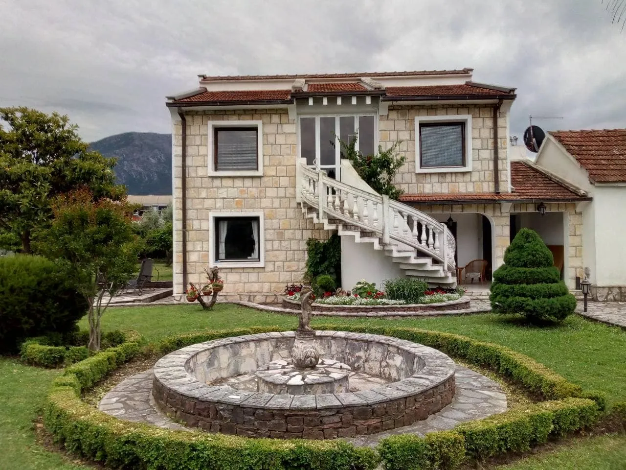 Stone house exterior with white staircase and circular fountain in the garden.