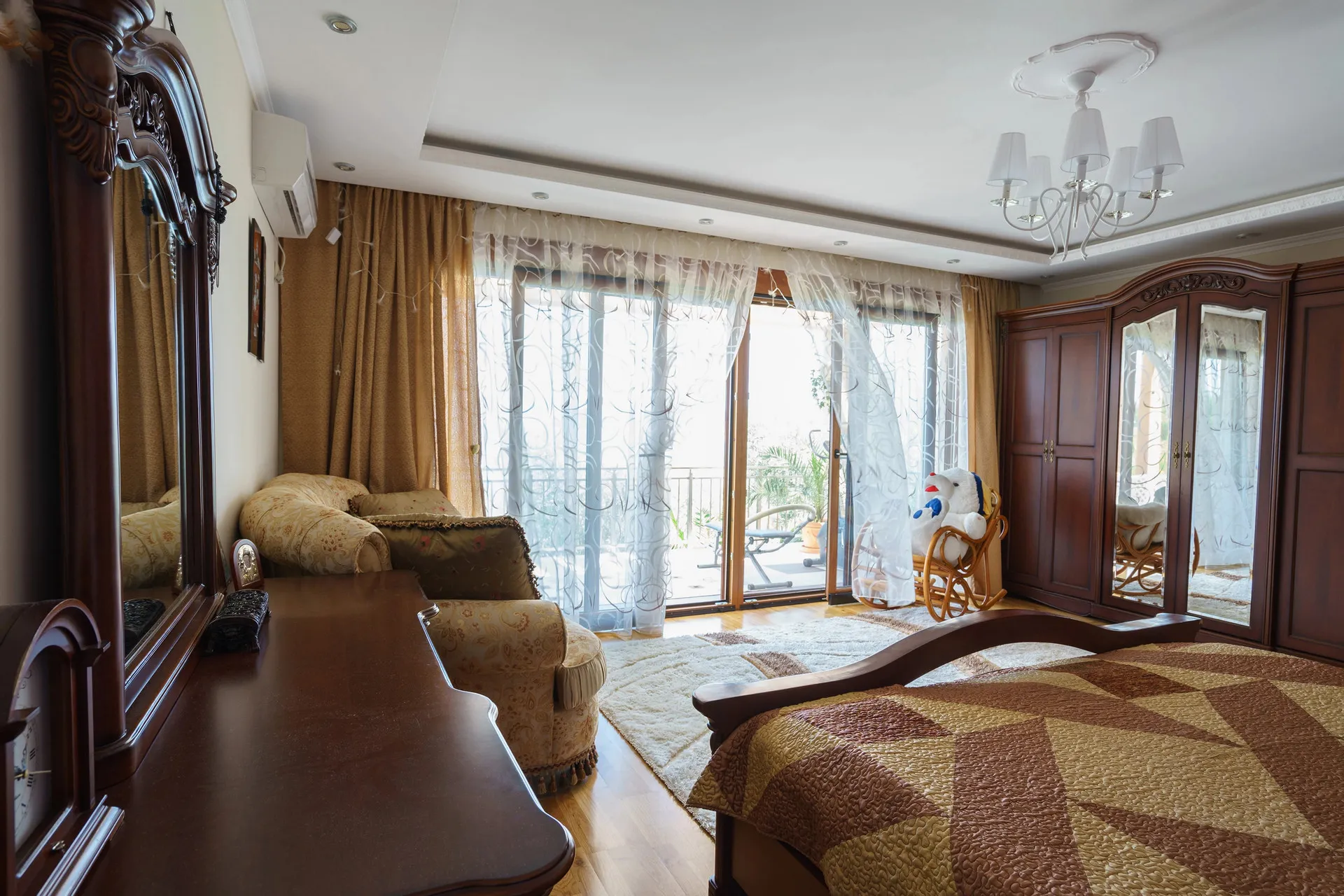 Bedroom featuring a wooden bed, wardrobe, and sofa near a balcony door with sheer curtains.