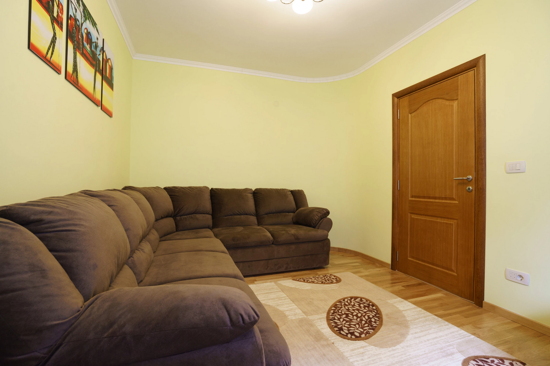 Living room with a brown corner sofa in a house in Sutomore, Montenegro: light walls, a wooden door, and parquet flooring.