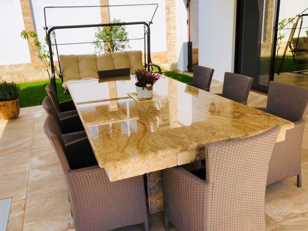 House terrace in Dobri Vody, Montenegro: dining table with a stone top, wicker chairs, and a garden swing.