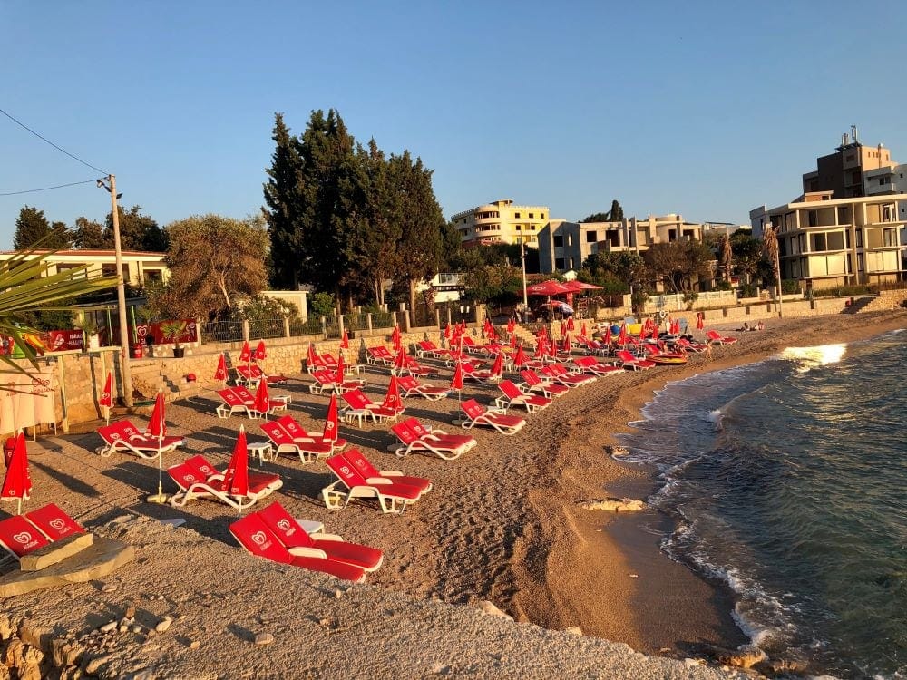 View of the equipped beach with red sun loungers and umbrellas by the sea in Dobre Vode, Montenegro.