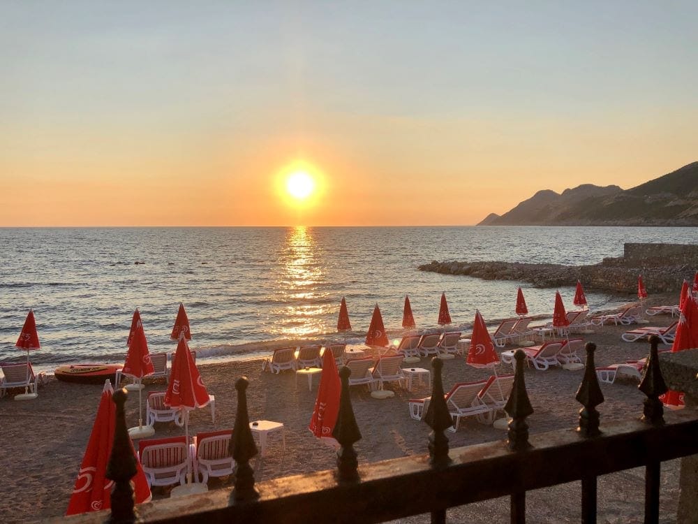 View of a sea beach with sun loungers and red umbrellas at sunset, house in Dobri Vody, Montenegro.