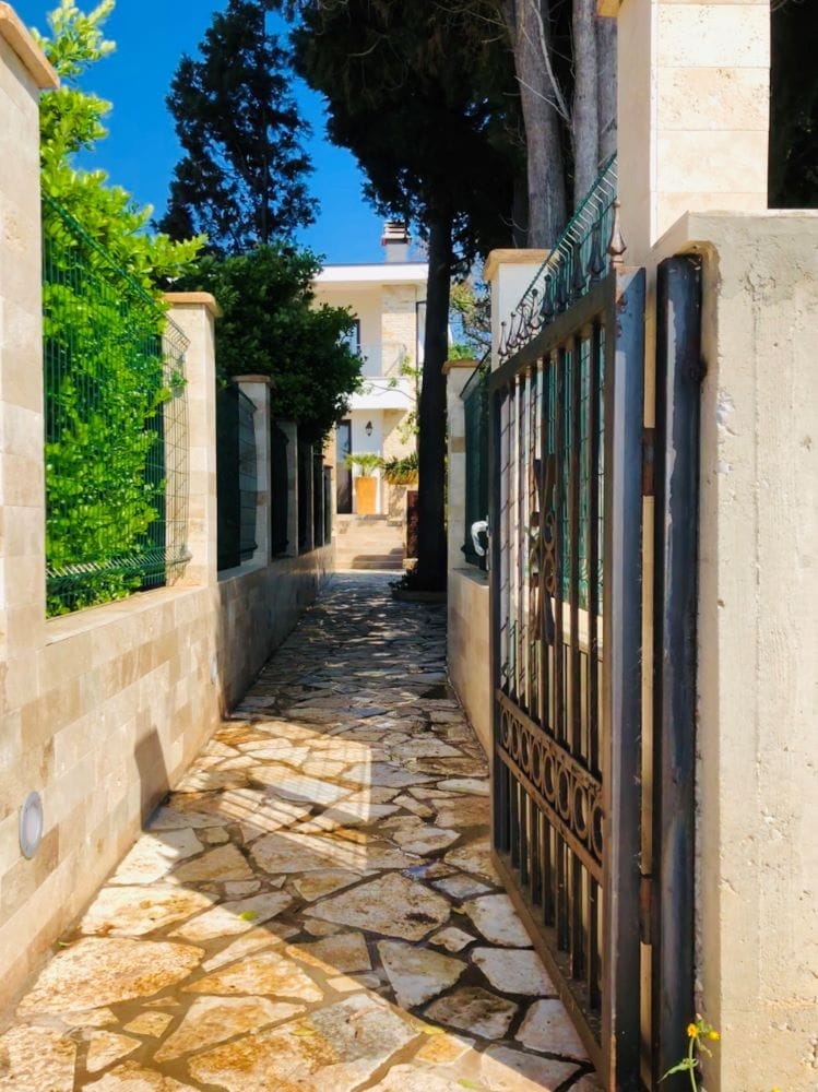 Entrance to the house in Dobri Vody, Montenegro: stone path, wrought-iron gate, and well-kept villa grounds.