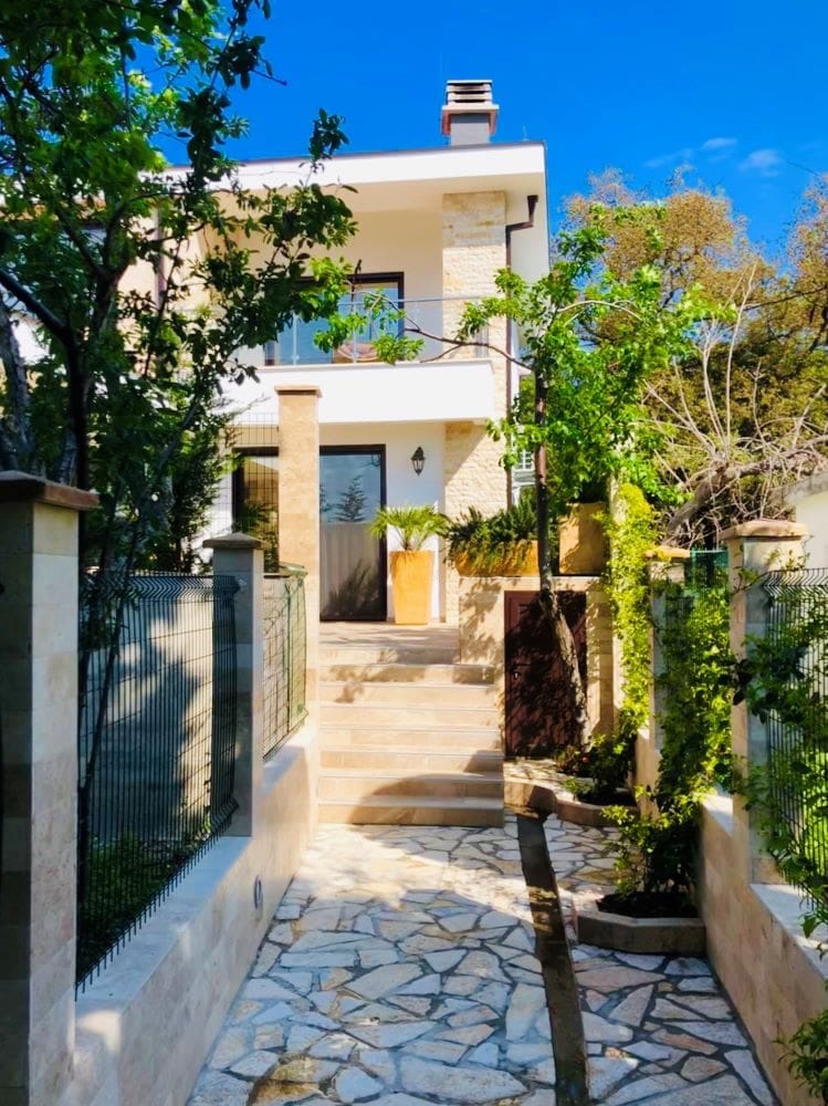 Modern villa in Dobra Voda, Montenegro: stone-clad facade, terrace, and landscaped entrance to the house.