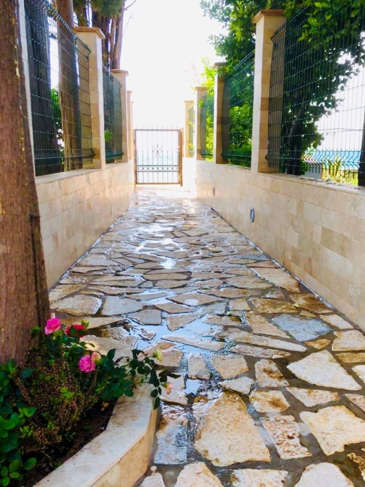 Stone path to the house in Dobri Vody, Montenegro: landscaped grounds with fencing and a flower bed.