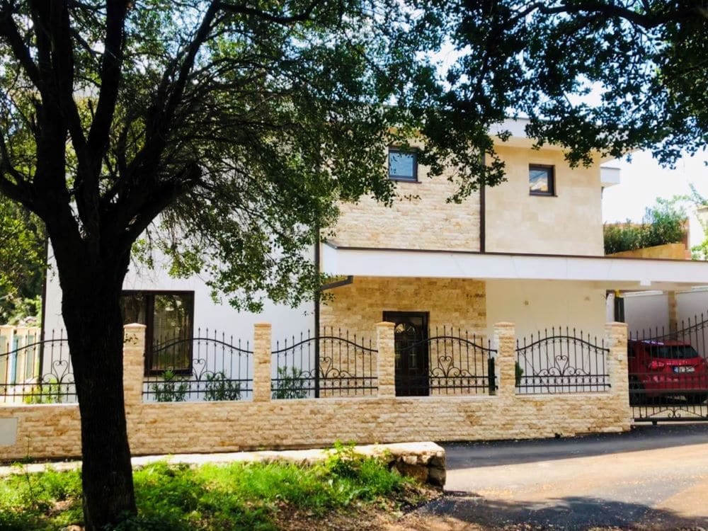 Modern house with stone cladding and a wrought-iron fence in Dobri Vody, Montenegro: front view and parking area.