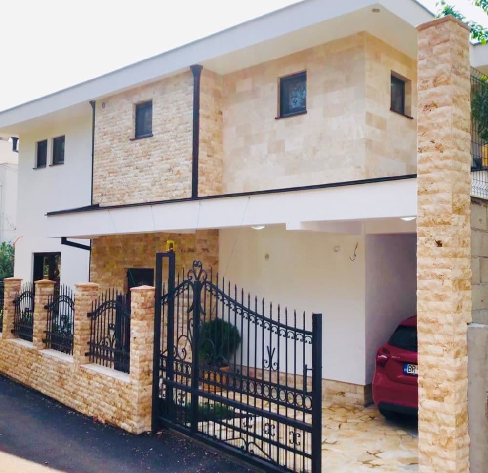 Modern house in Dobri Vody, Montenegro: stone facade, wrought-iron gate, carport, and courtyard parking.