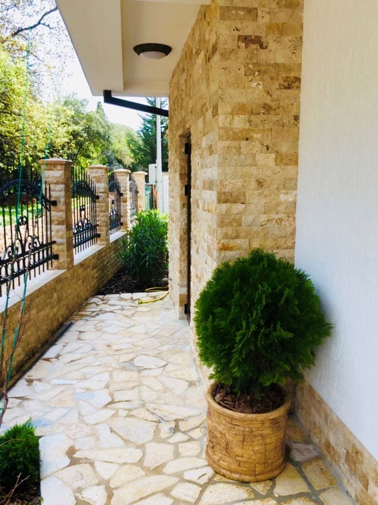 Terrace of a house in Dobri Vody, Montenegro: natural stone finish, wrought-iron fence, and landscaping with thuja trees.