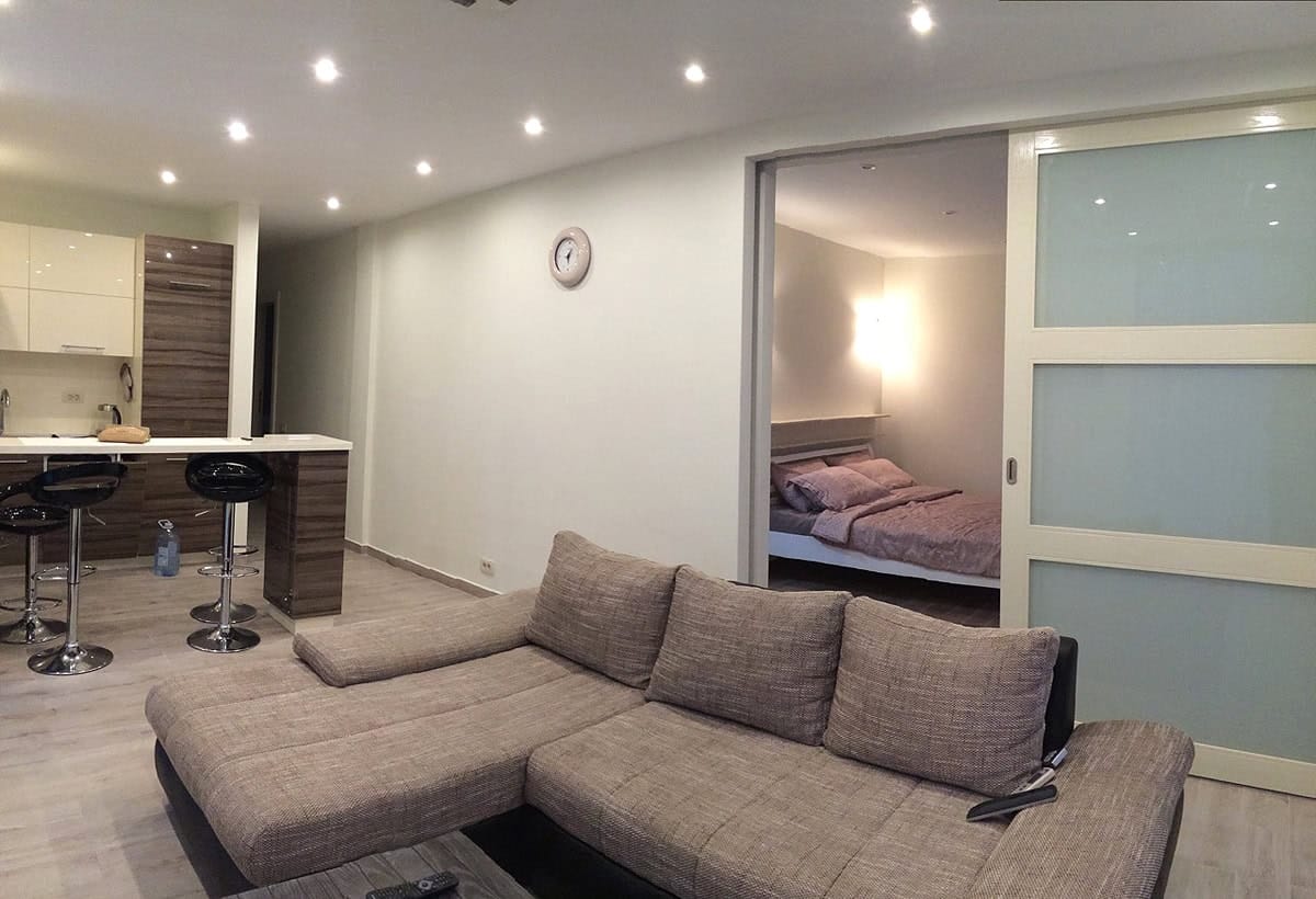 Interior of a living room with kitchen and bedroom in an apartment, Prčanj, Montenegro: corner sofa, bar counter, and sliding doors.