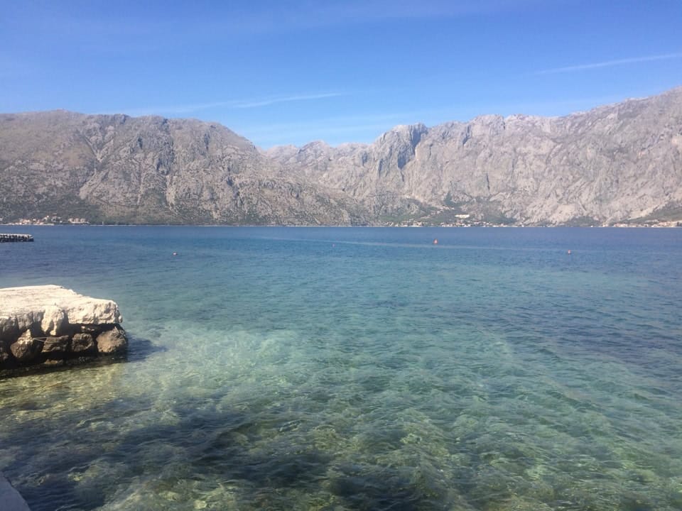 Panoramic view of the Bay of Kotor and mountains from an apartment in Prčanj, Montenegro: clear water and a stone pier.