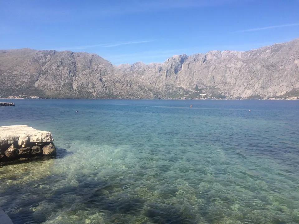 Scenic view of a mountain bay with clear turquoise water, rocky shore, and blue sky.