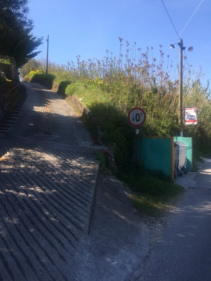 Access road to the residential complex in Prčanj, Montenegro: paved entrance with a road sign and containers.