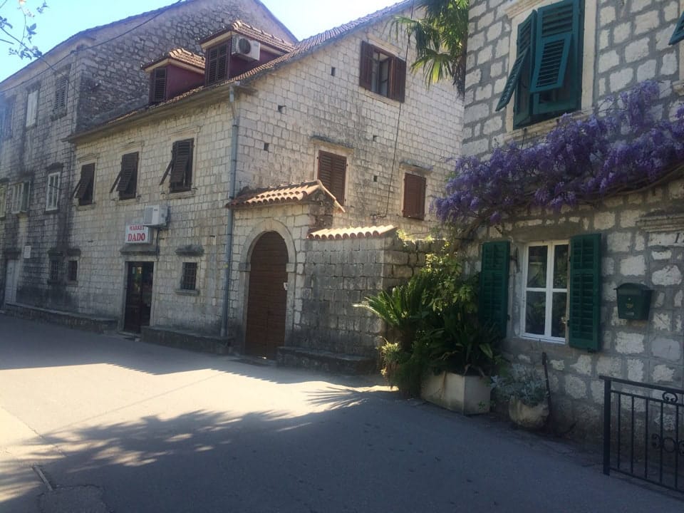 Traditional stone house in Prčanj, Montenegro: historic architecture, green shutters, and blooming wisteria.