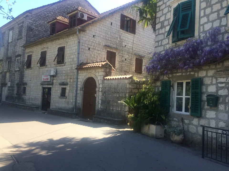 Stone houses with wooden shutters and purple flowers on a street.