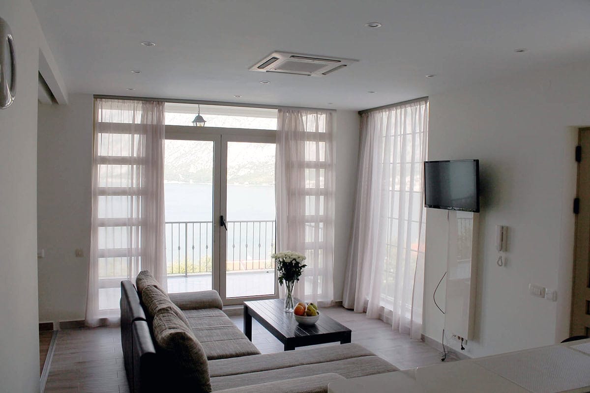 Living room with panoramic sea view in an apartment, Prčanj, Montenegro: modern interior, sofa, and access to the balcony.