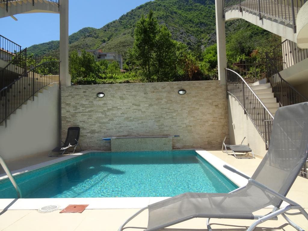 Outdoor pool with sun loungers and stone wall finish at the apartments in Prčanj, Montenegro, mountain view.