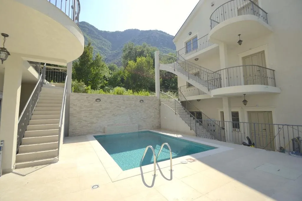 Outdoor swimming pool with metal ladder, surrounded by white building and mountains.