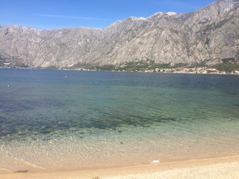 Panoramic view of the sea and mountains from the beach in Prčanj, Montenegro, with coastal properties and a clear bay in the background.