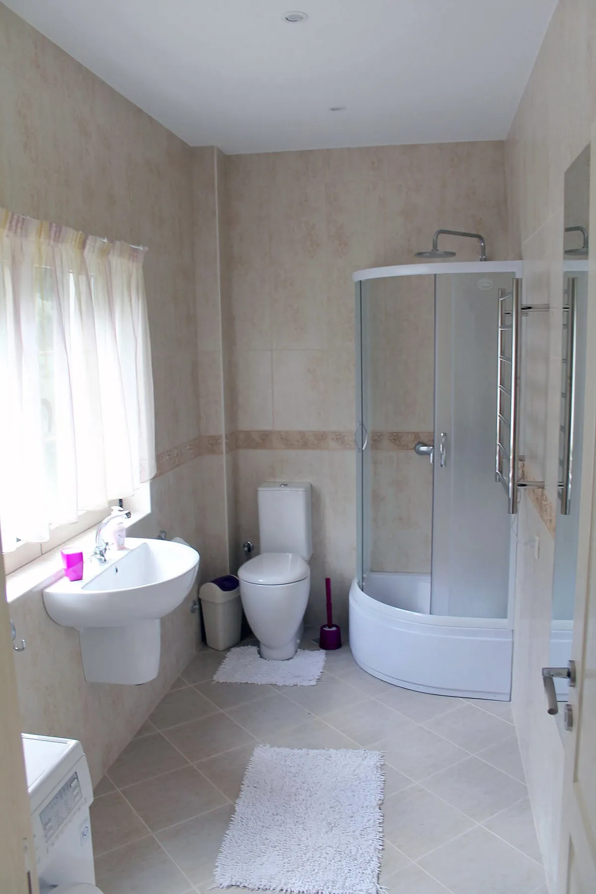 Bathroom featuring a corner shower enclosure, toilet, wall-mounted sink, and beige tiled walls.