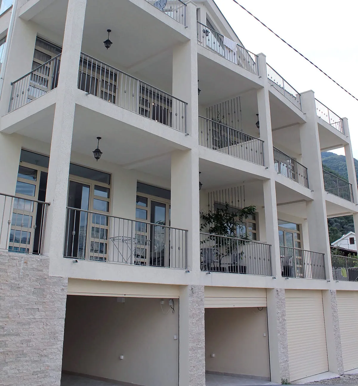 Exterior view of a multi-story residential building featuring balconies with metal railings and ground-floor garage doors.