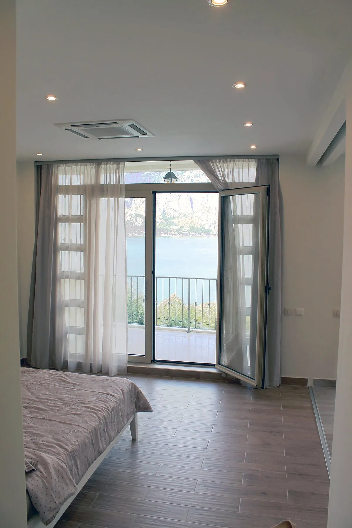 Bedroom with a bed, wood-look floor, and open door leading to a balcony overlooking water.