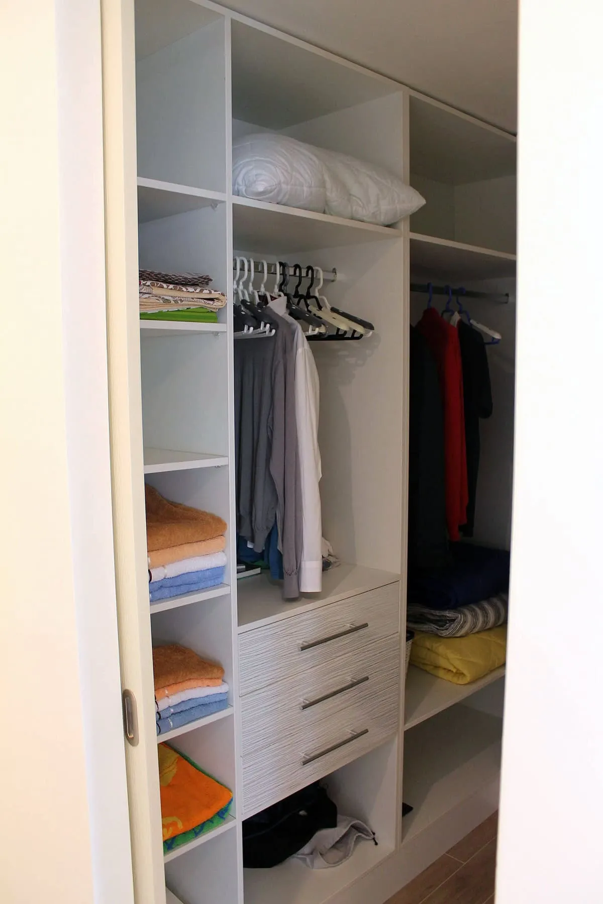 Built-in white wardrobe with shelves, drawers, and hanging rods for clothes and towels.