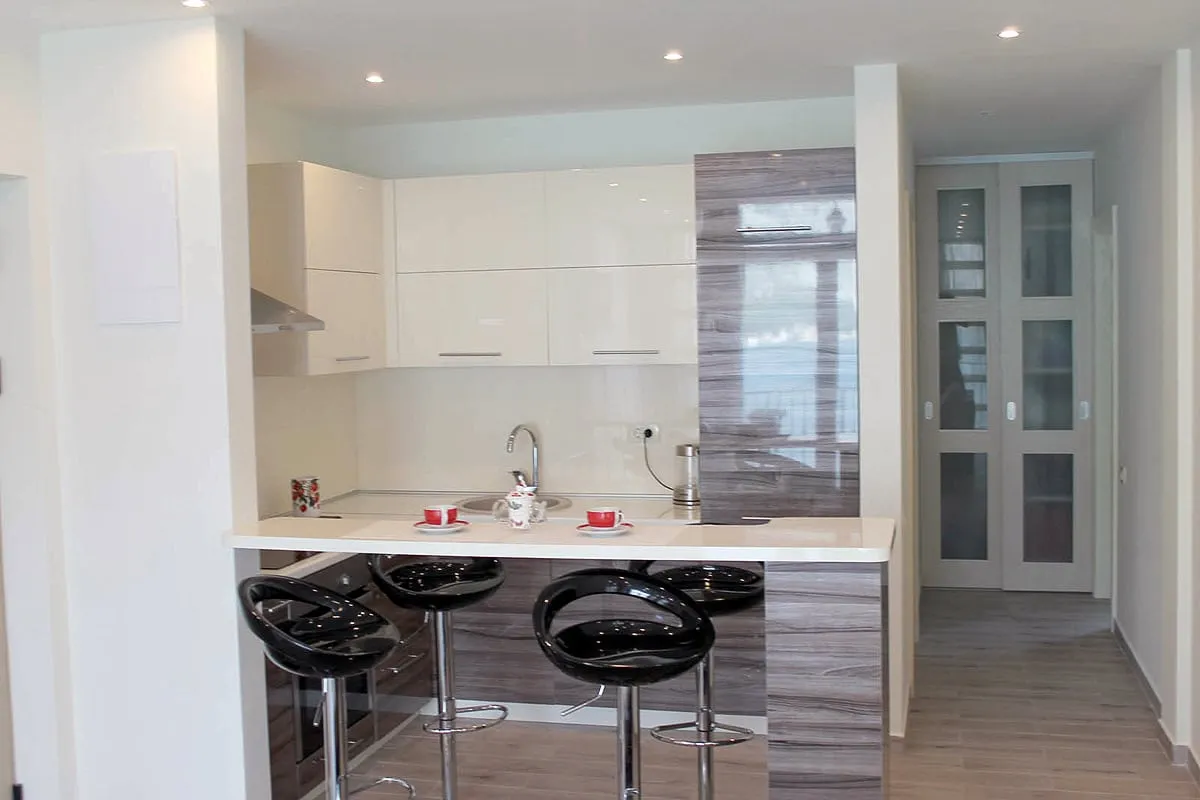 Modern kitchen with white glossy cabinets, a breakfast bar, and black high stools.