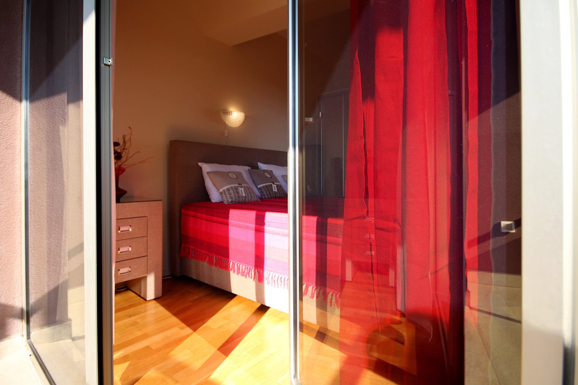 Cozy bedroom with a double bed and red curtains in an apartment in Bečići, Montenegro.