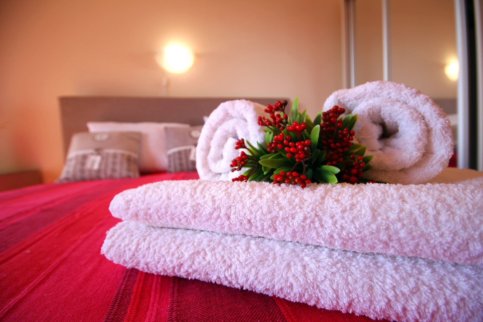 Cozy bedroom in an apartment in Bečići, Montenegro: a double bed with a red bedspread and white towels.