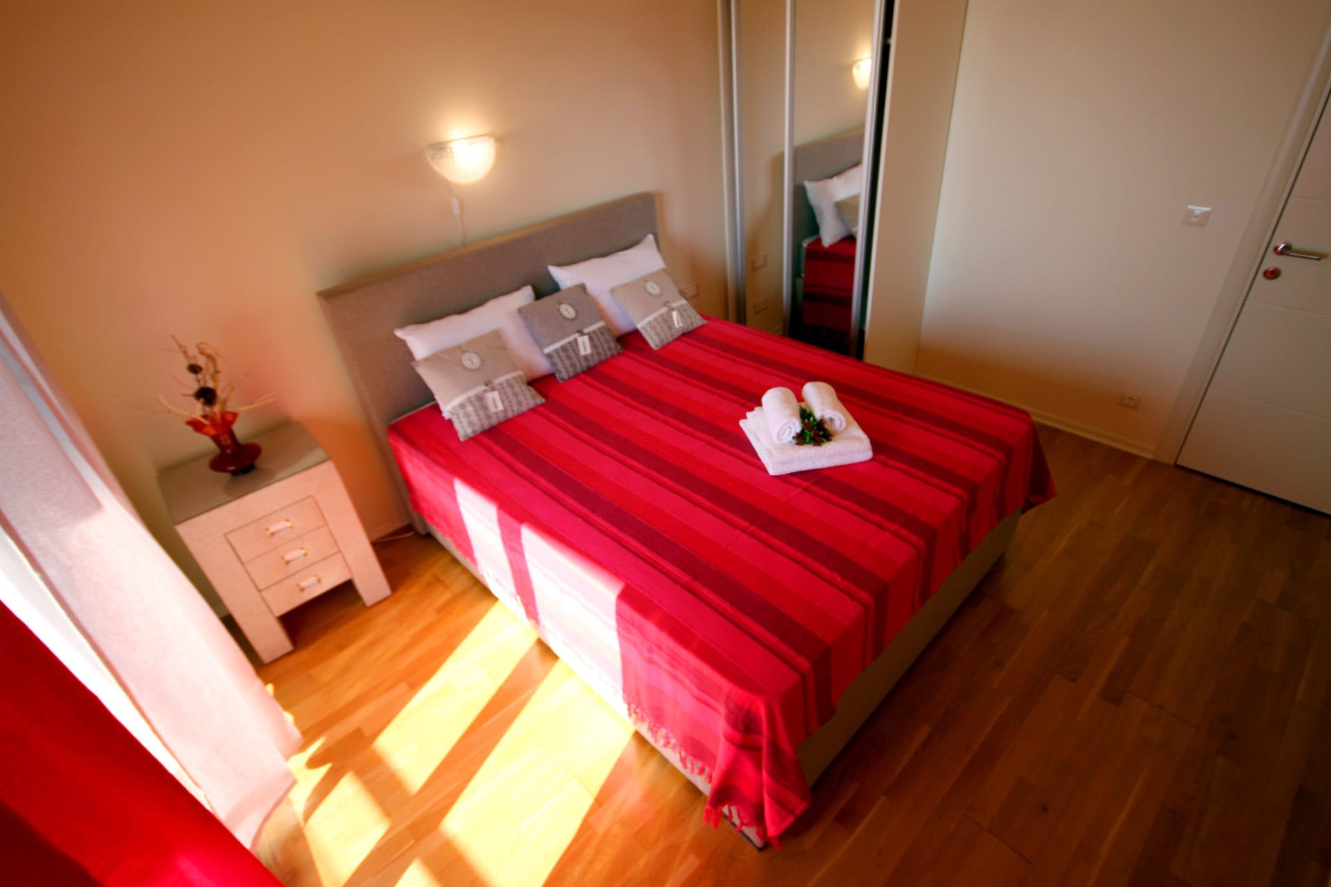 Cozy bedroom with a double bed in an apartment in Bečići, Montenegro: bright interior, parquet flooring, and a mirrored wardrobe.