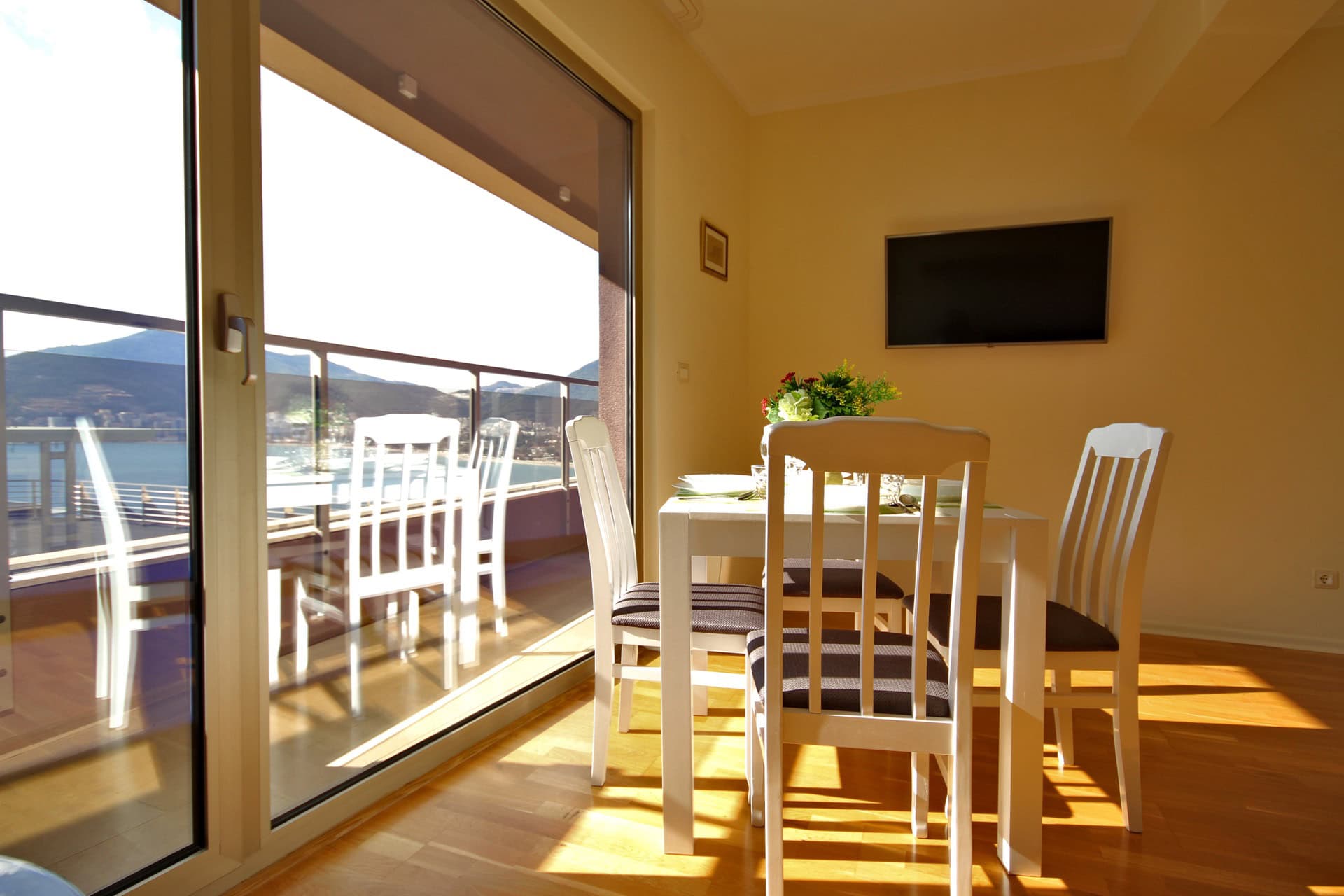 Living room with dining area in an apartment in Bečići, Montenegro: panoramic windows, sea view, and access to the terrace.
