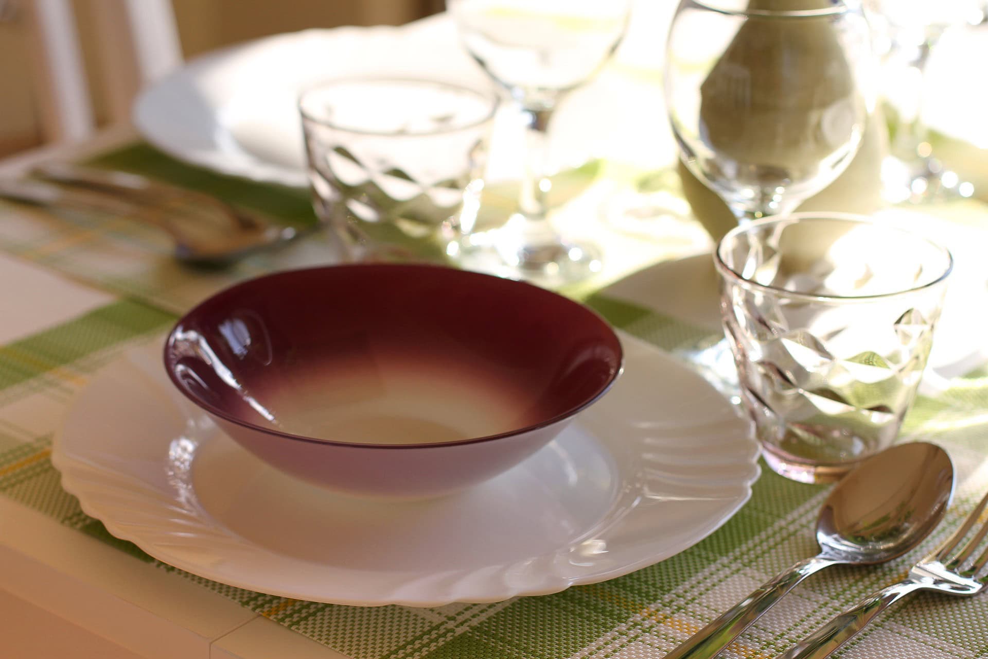 Table setting with dishes in an apartment interior in Bečići, Montenegro: a white plate, a burgundy bowl, and glasses.