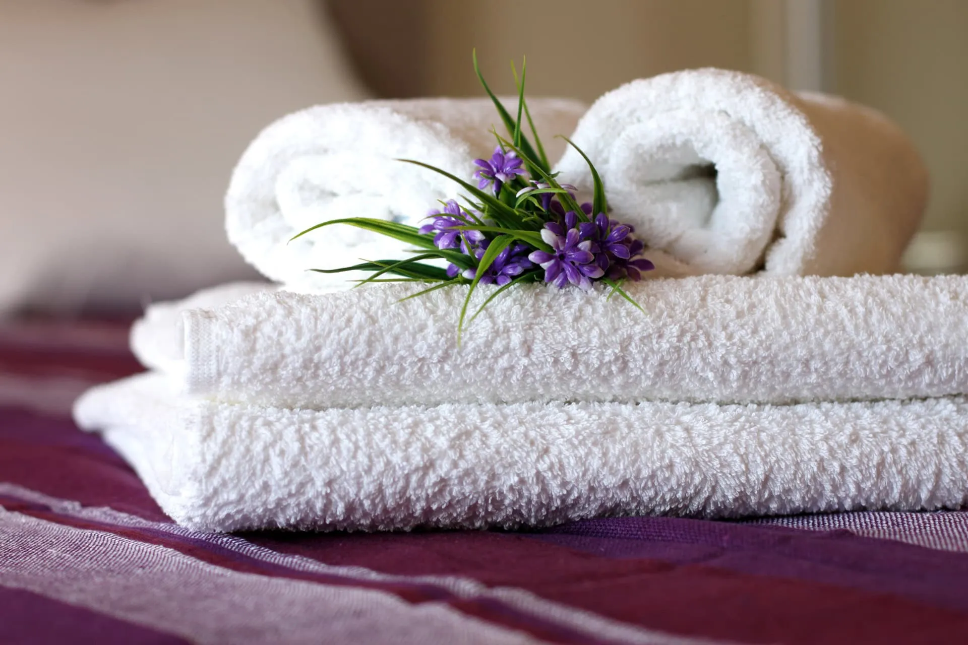 Stacked white towels with purple flowers rest on maroon bedding; no specific room features are visible.