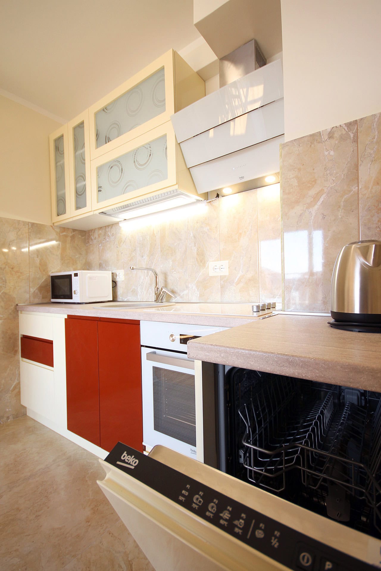 Modern kitchen in an apartment in Bečići, Montenegro: built-in Beko appliances, light cabinet fronts, and a marble backsplash.