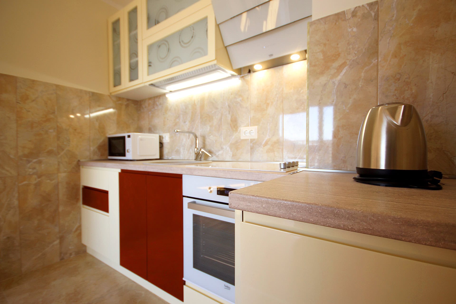 Modern kitchen in an apartment in Bečići, Montenegro: built-in appliances, glossy fronts, and marble-look tile finishes.