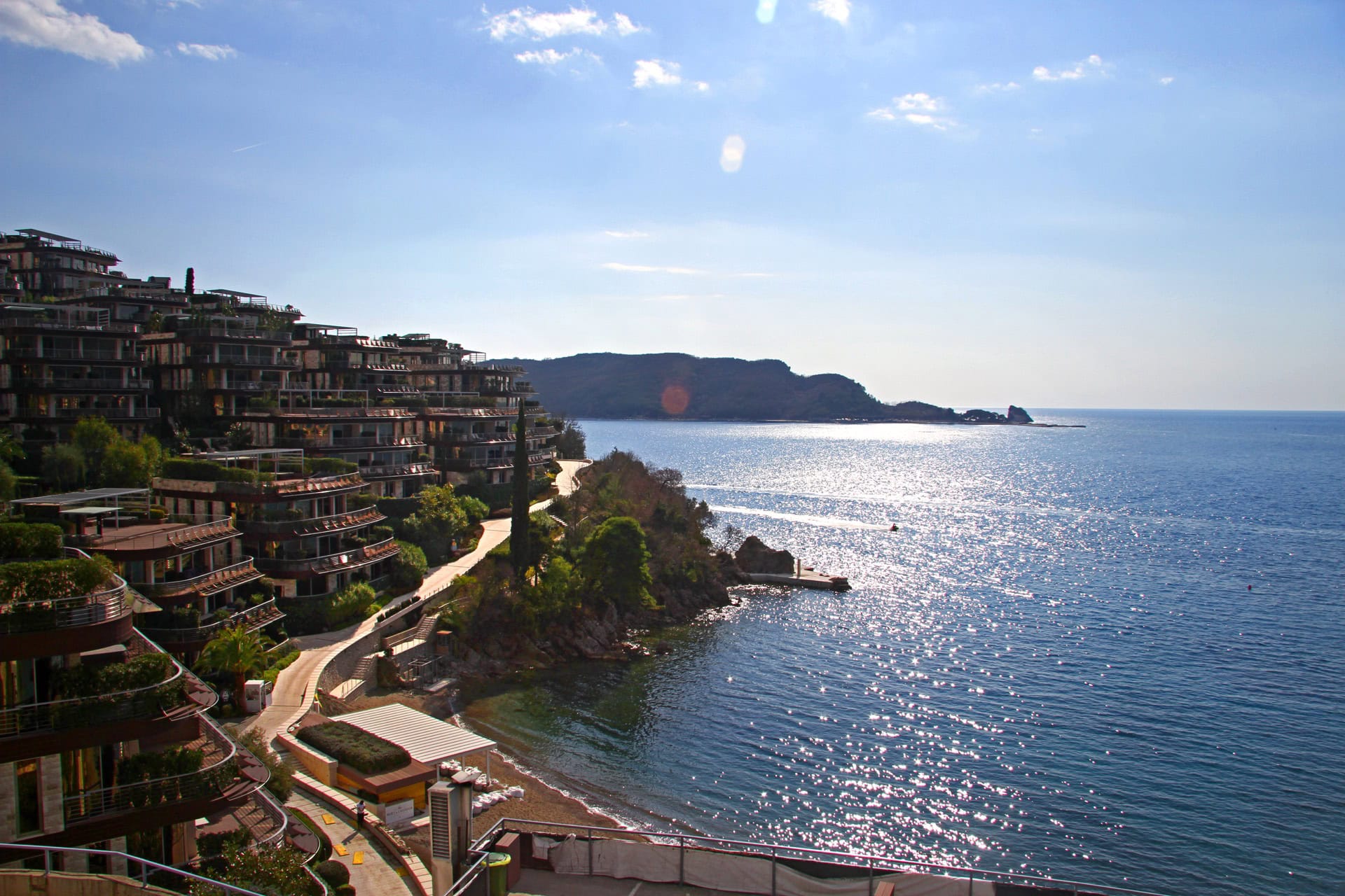 View of a luxury residential complex by the sea in Bečići, Montenegro: modern terraces, private beach, and a panoramic view of the Adriatic.